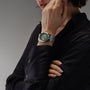 A person in a black shirt displays the Raymond Weil Freelancer Automatic Olive Green Dial watch, hand near chin, against a neutral background.