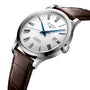 The Longines Record features a silver case, white dial with black Roman numerals, blue hands, date at 3 o’clock, brown leather strap, “Automatic Chronometer” inscription, and a silicon balance spring.