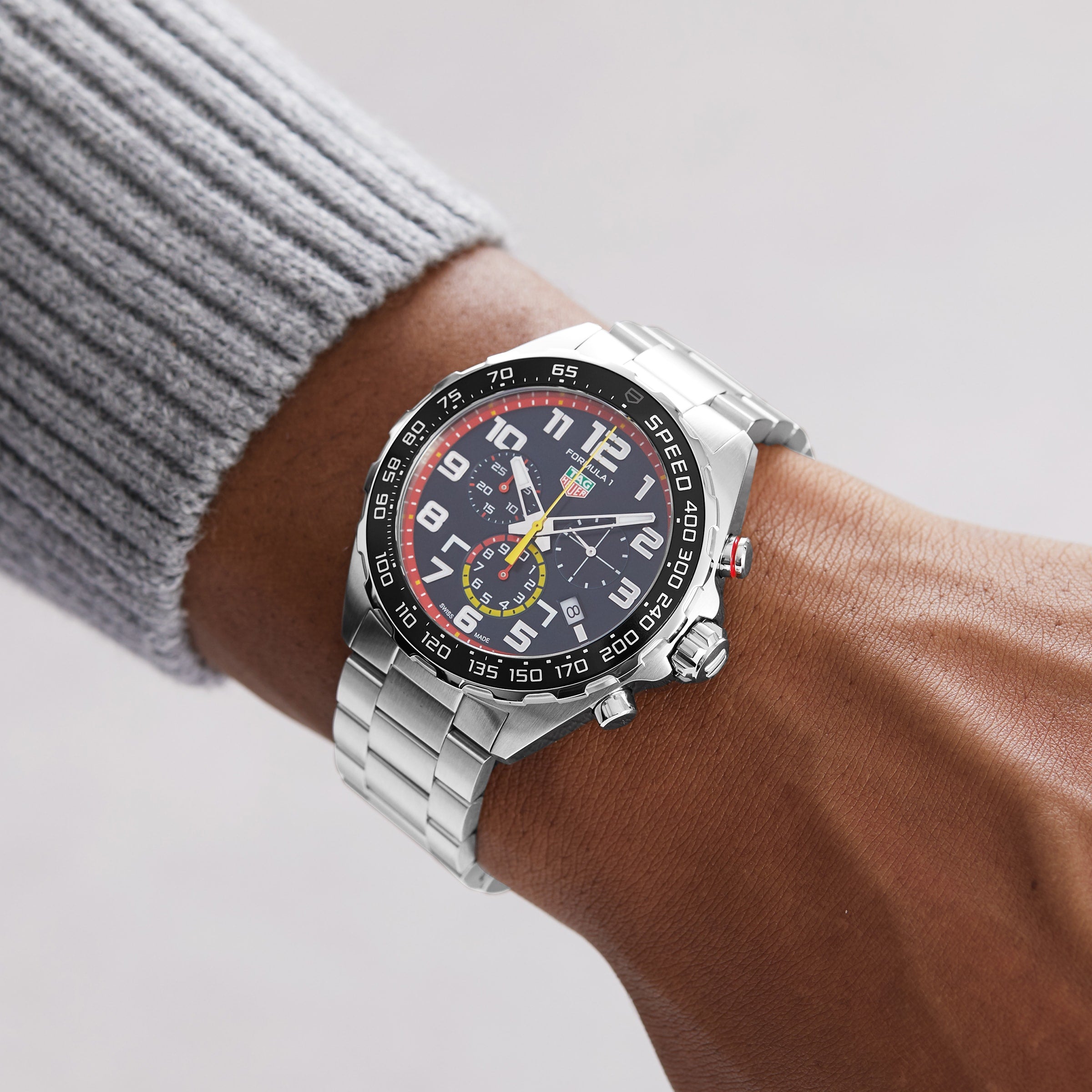 A person wearing a TAG Heuer Special Edition Formula 1 Chronograph x Red Bull Racing watch with a black multi-dial face and white numerals on their left wrist, set against a neutral background.