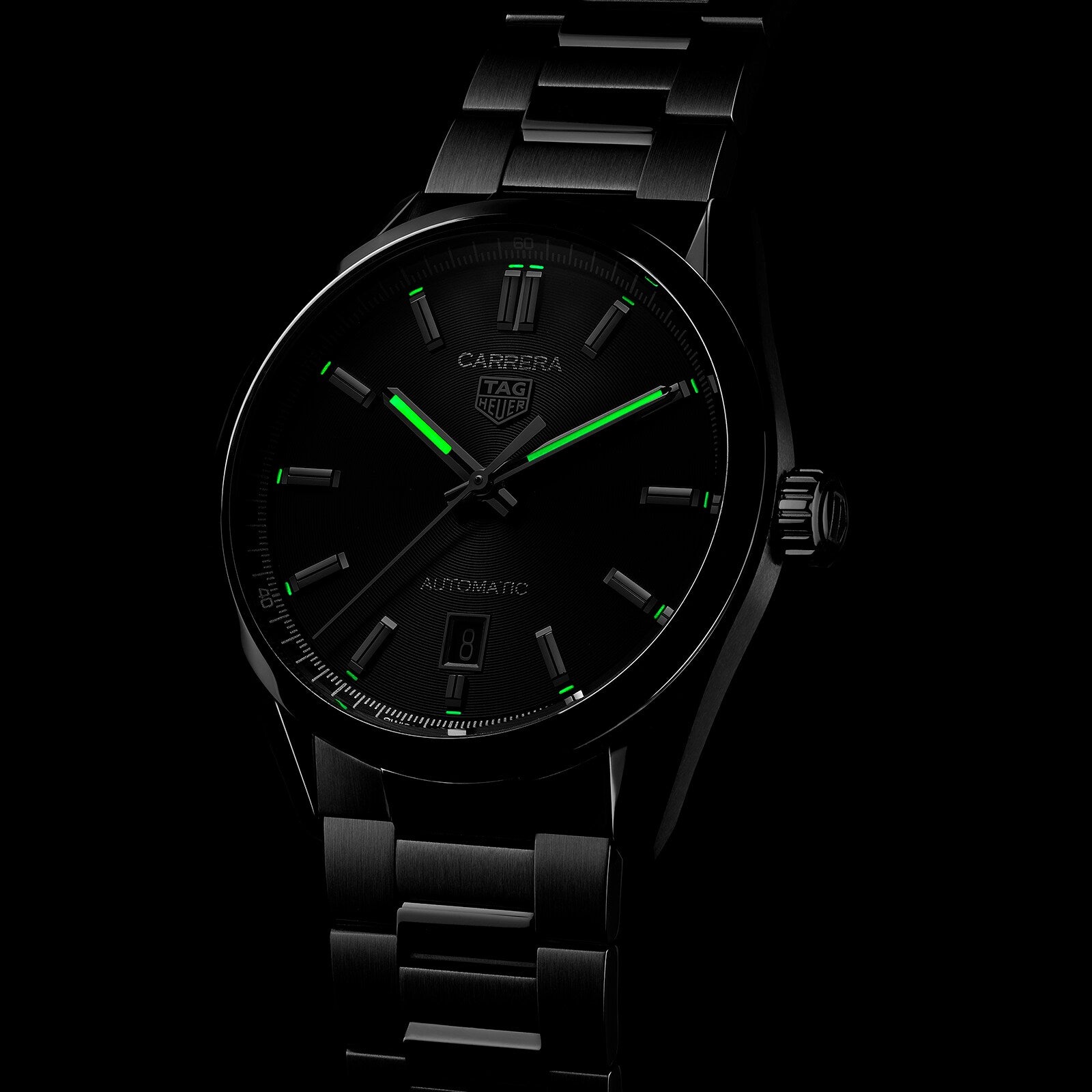 The TAG Heuer Carrera Date is a black watch with Calibre 5 automatic movement and a metal bracelet, featuring green luminescent hour markers and hands set against a dark background.