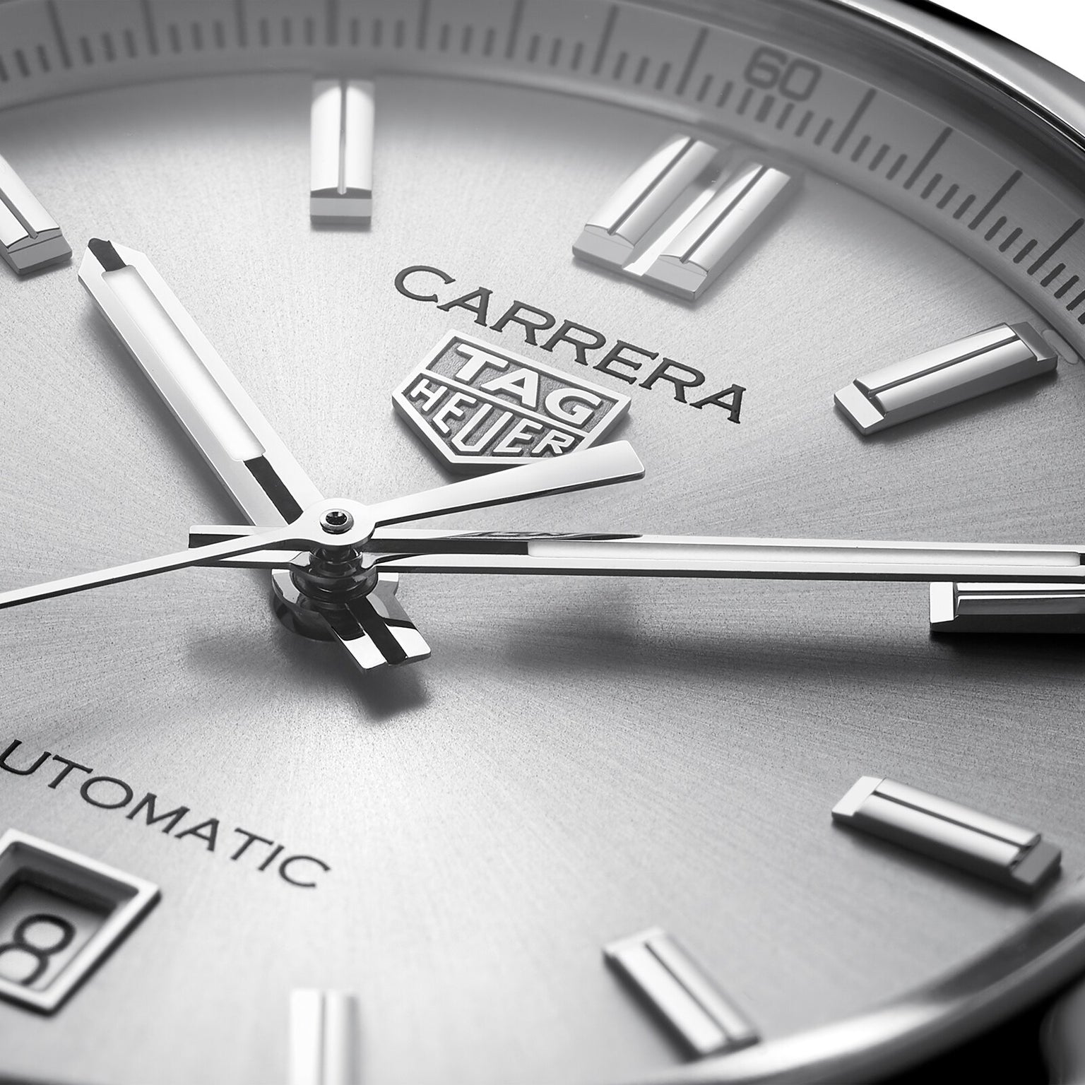 Close-up of the TAG Heuer Carrera Date watch face with silver markers, hands, and branding. The date window is visible, reflecting the legacy of the Carrera Panamericana race.