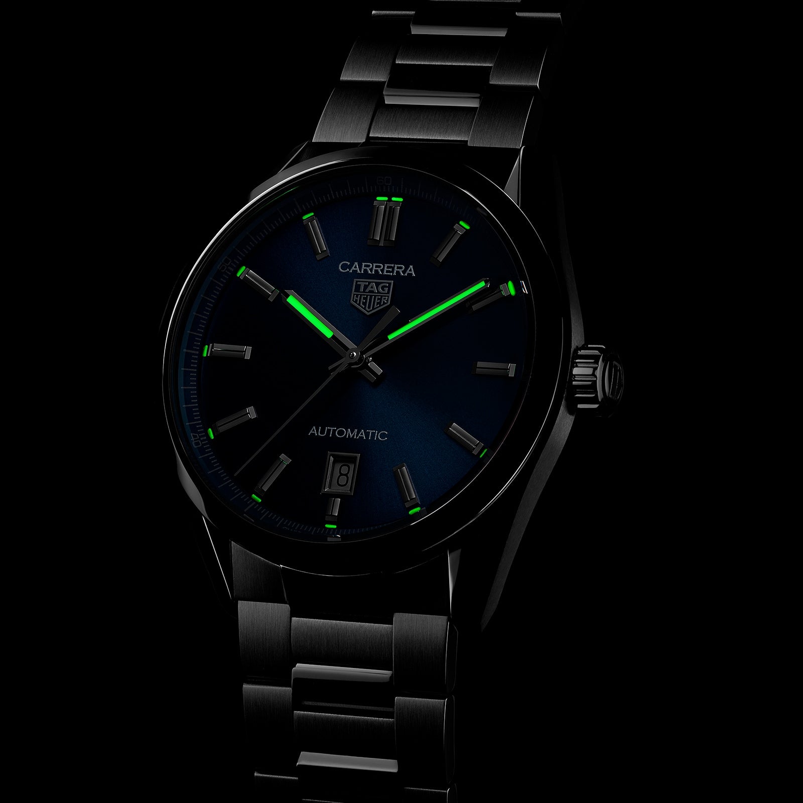 The TAG Heuer Carrera Date watch, featuring a dark dial, luminescent green markers, and a stainless steel bracelet, is showcased against a black background.