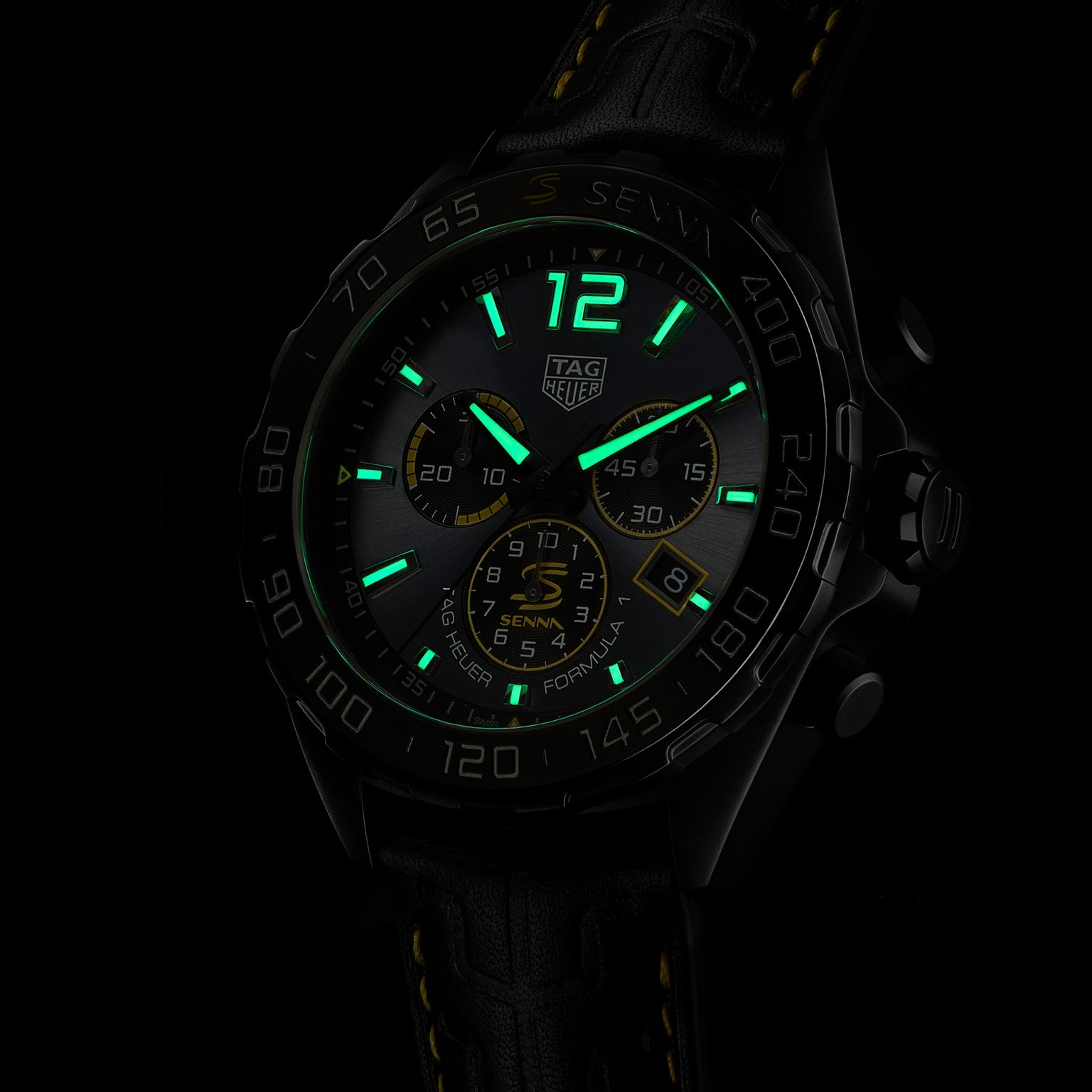 The TAG Heuer Special Edition Formula 1 Senna wristwatch features luminescent green markers and hands, a black case, leather strap with yellow stitching, and multiple subdials, all inspired by Ayrton Senna and shown in a dark setting.