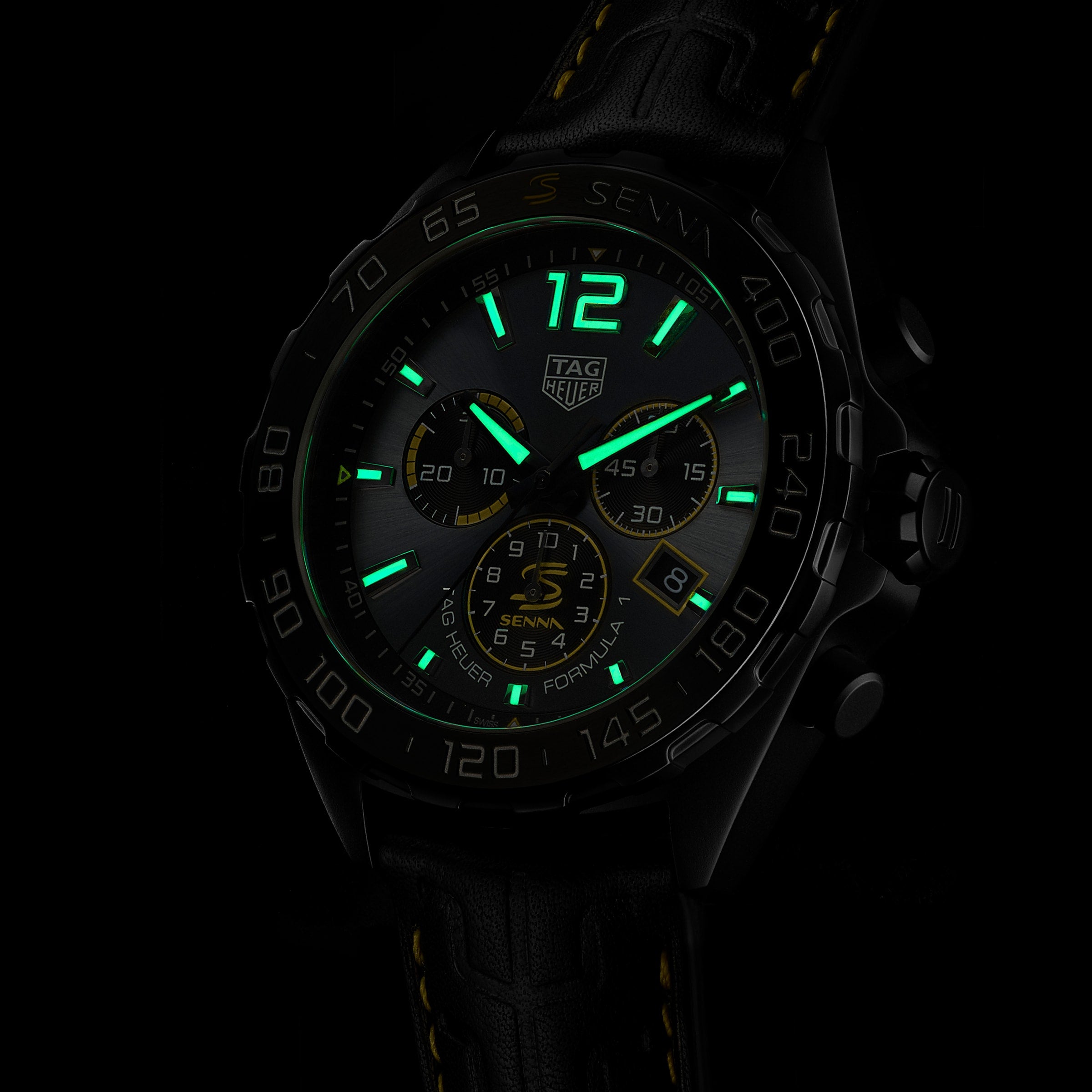 The TAG Heuer Special Edition Formula 1 Senna wristwatch features luminescent green markers and hands, a black case, leather strap with yellow stitching, and multiple subdials, all inspired by Ayrton Senna and shown in a dark setting.