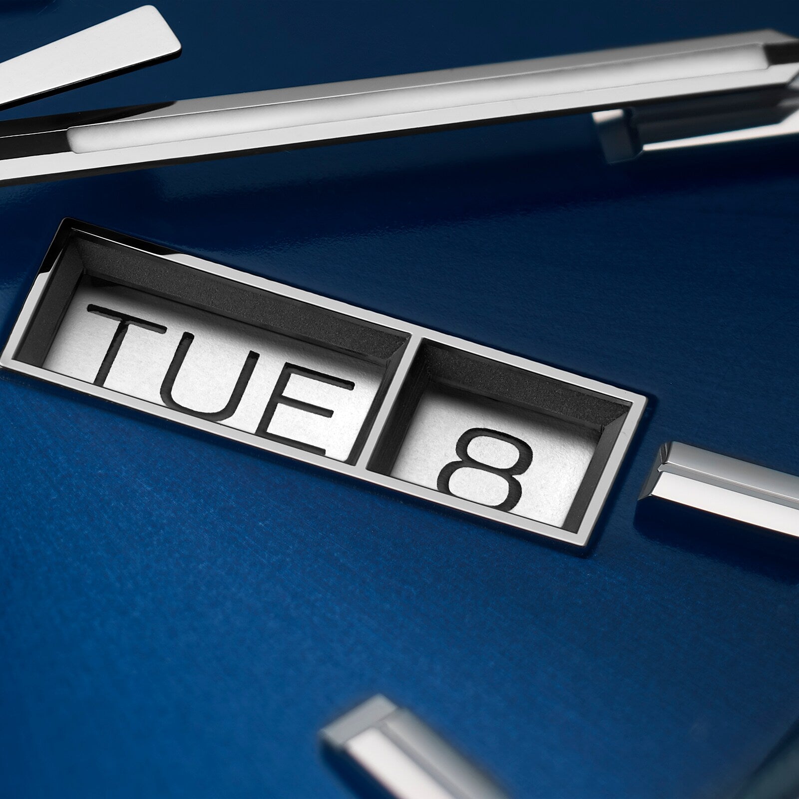 Close-up of the TAG Heuer Carrera Day-Date watch face showing TUE and 8 on a blue background, with metallic hands and markers—highlighting its Calibre 5 automatic movement.