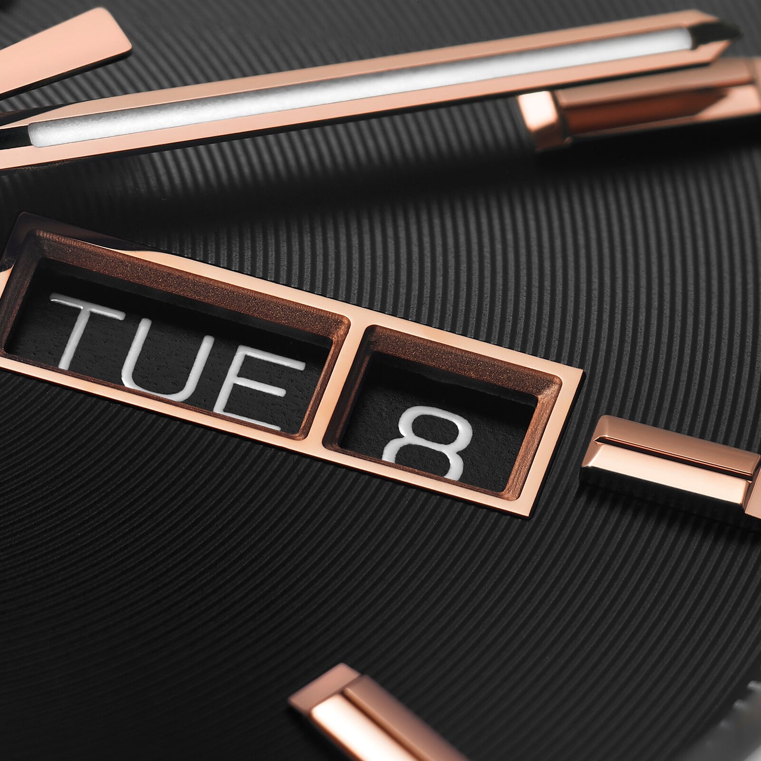 Close-up of the TAG Heuer Carrera Day-Date watch face featuring rose gold hour markers and hands, a day-date window showing TUE 8, and a textured black background for a look of refined luxury.