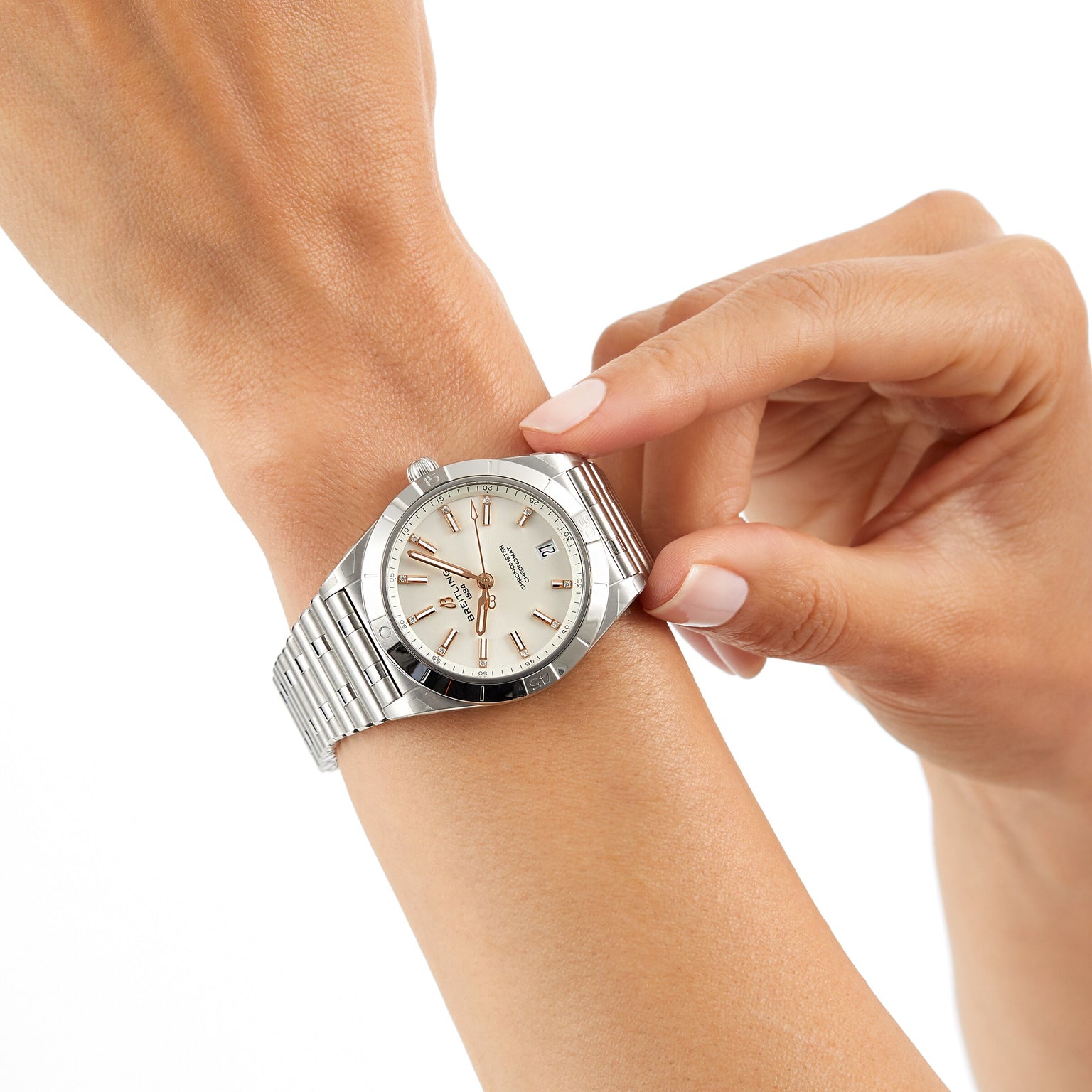 A person adjusts a Breitling Chronomat Automatic 36 wristwatch with a silver case, white dial, and signature Rouleaux bracelet on their left wrist against a plain white background.