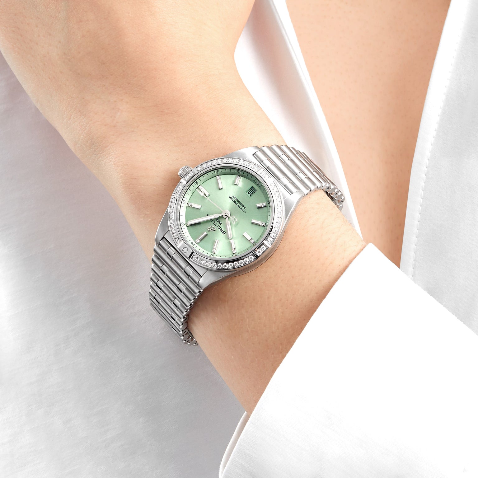 A Breitling Chronomat Automatic 36 wristwatch with a light green face, diamond hour markers, and a diamond-set bezel is worn on the wrist, paired with a white long-sleeve shirt.