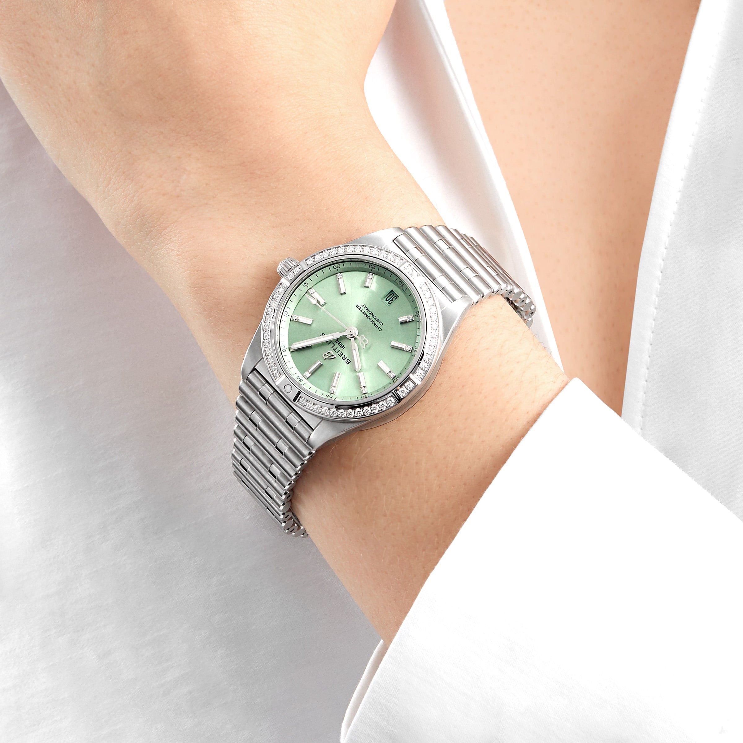 A Breitling Chronomat Automatic 36 wristwatch with a light green face, diamond hour markers, and a diamond-set bezel is worn on the wrist, paired with a white long-sleeve shirt.