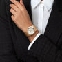 A person in a black textured blazer and white shirt wears a Breitling Chronomat Automatic 36 wristwatch with a COSC certified movement, white dial, simple hour markers, and an elegant Rouleaux bracelet.