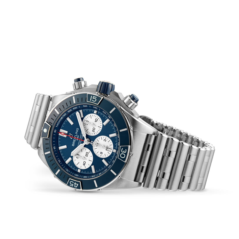A Breitling Super Chronomat B01 44 stainless steel chronograph wristwatch with a blue bezel, blue dial, three white subdials, and a metal bracelet is angled against a white background.