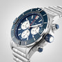 The Breitling Super Chronomat B01 44 is a stainless steel mechanical chronograph watch with a blue bezel and dial, three subdials, and a metal link bracelet, shown against a light background.