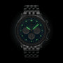 A Breitling Navitimer B01 Chronograph 46 wristwatch with a black dial and metal bracelet is shown in the dark, featuring glowing green luminescent hands and hour markers.