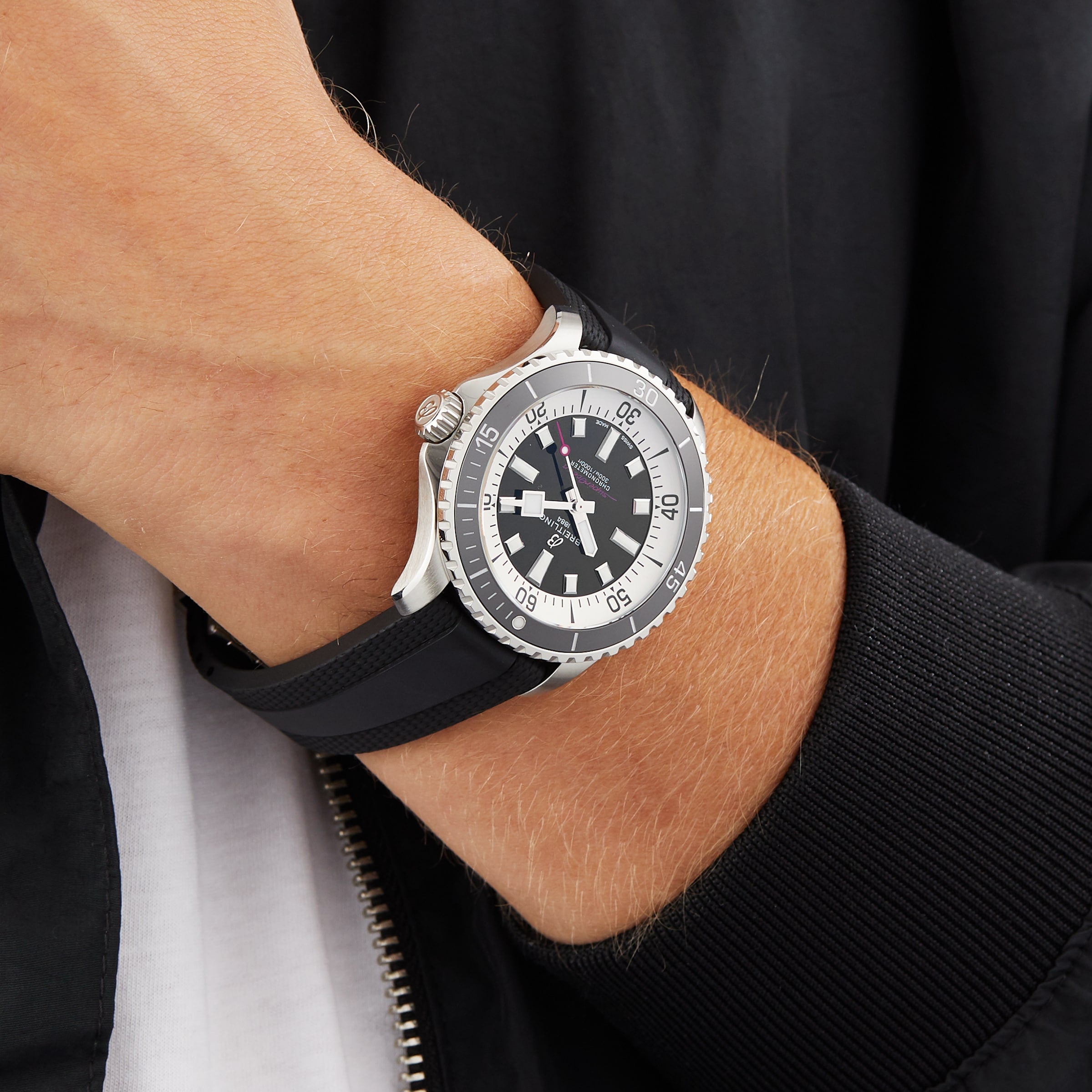 A person in a black jacket and white shirt wears a Breitling Superocean Automatic 44 featuring a black and white dial, black and silver case, and a black rubber strap.
