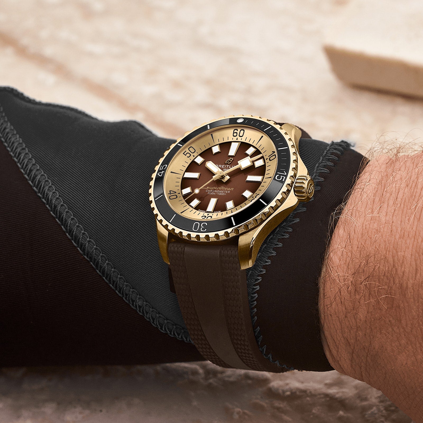 A close-up of a wrist wearing the Breitling Superocean Automatic 44, featuring a bronze case and brown strap, paired with a black wetsuit sleeve from the renowned Superocean collection.
