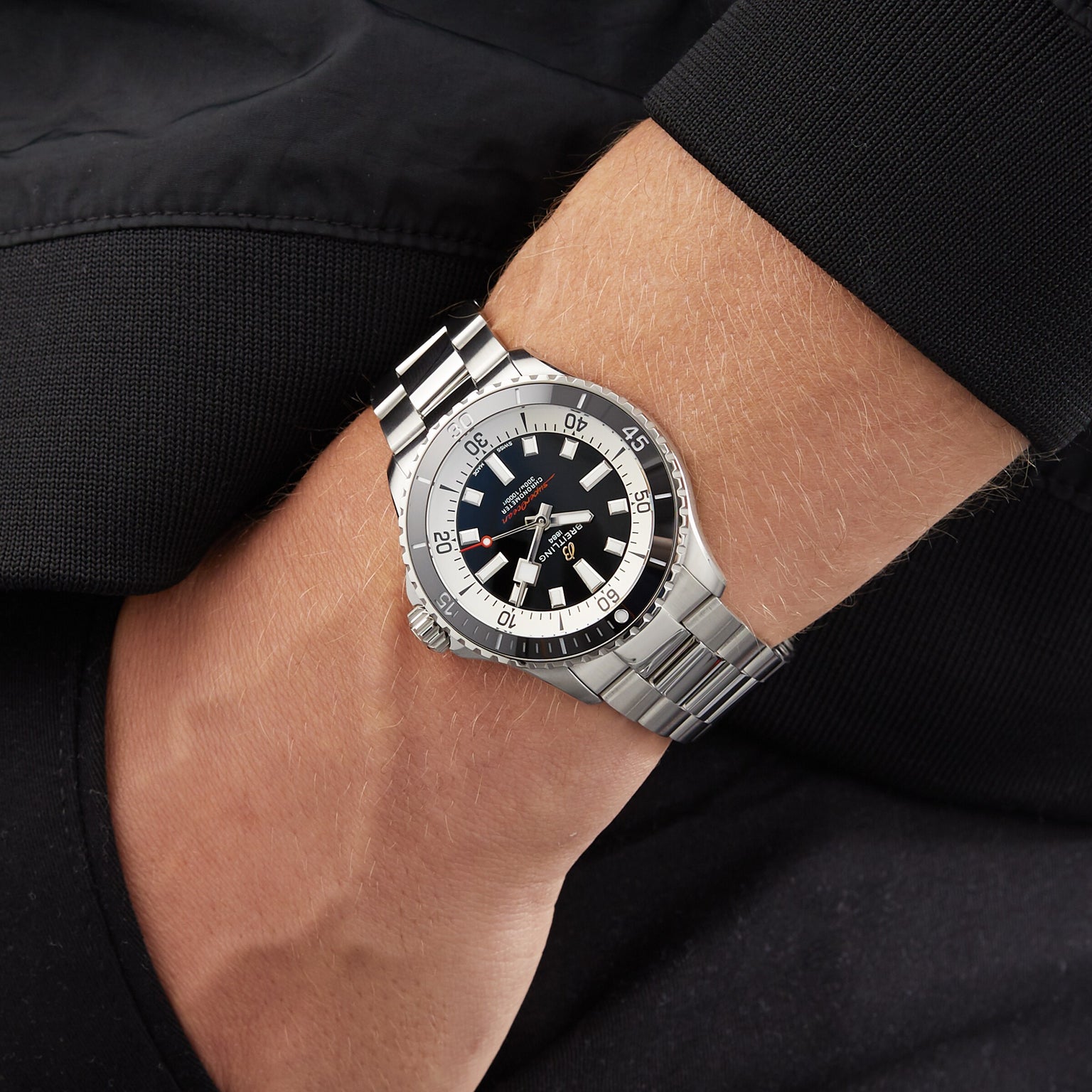 A Breitling Superocean Automatic 42 with a silver wristband and black dial is worn on a person’s wrist with a dark jacket.