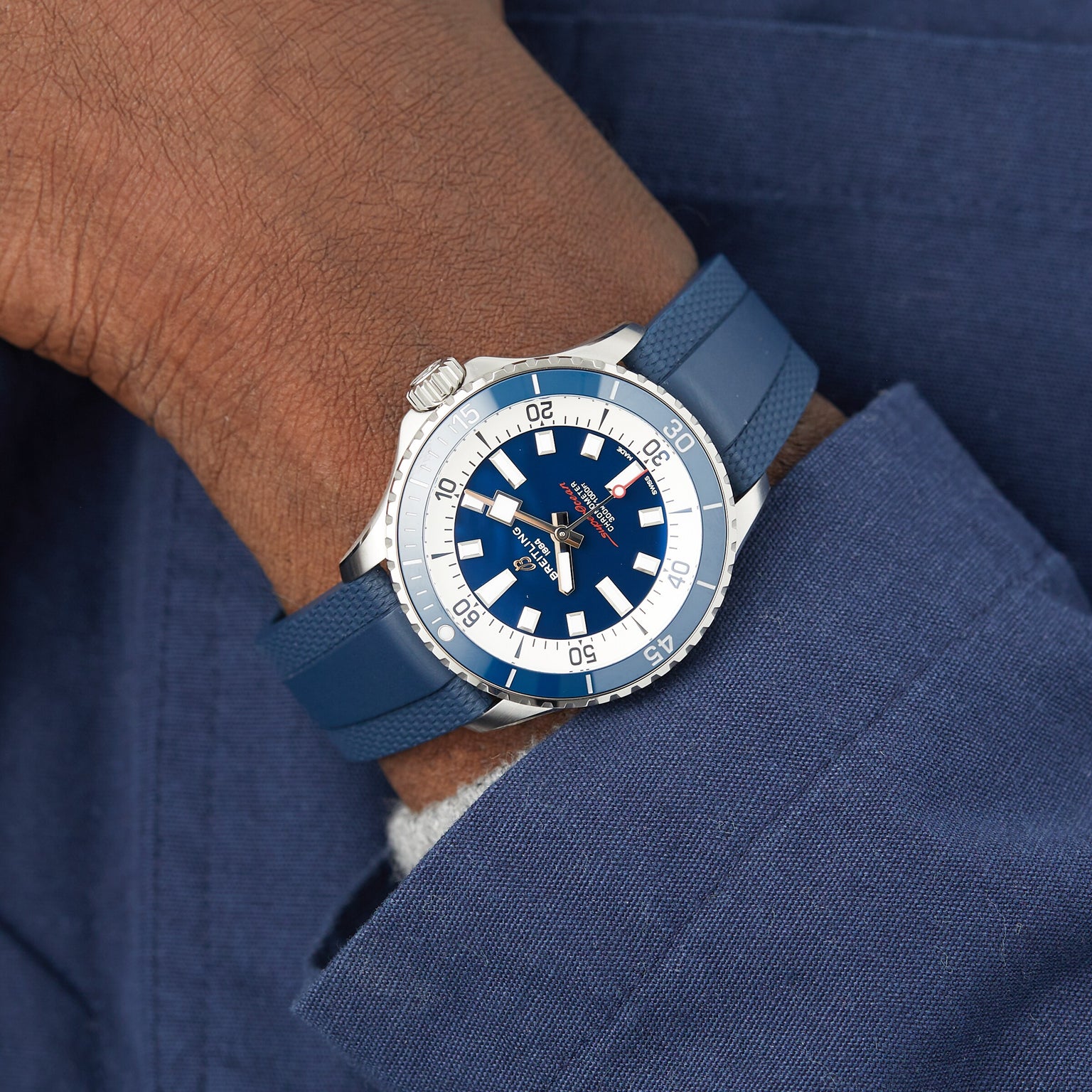 A person in a blue suit jacket wears a Breitling Superocean Automatic 42 dive watch with a blue dial and blue rubber strap.