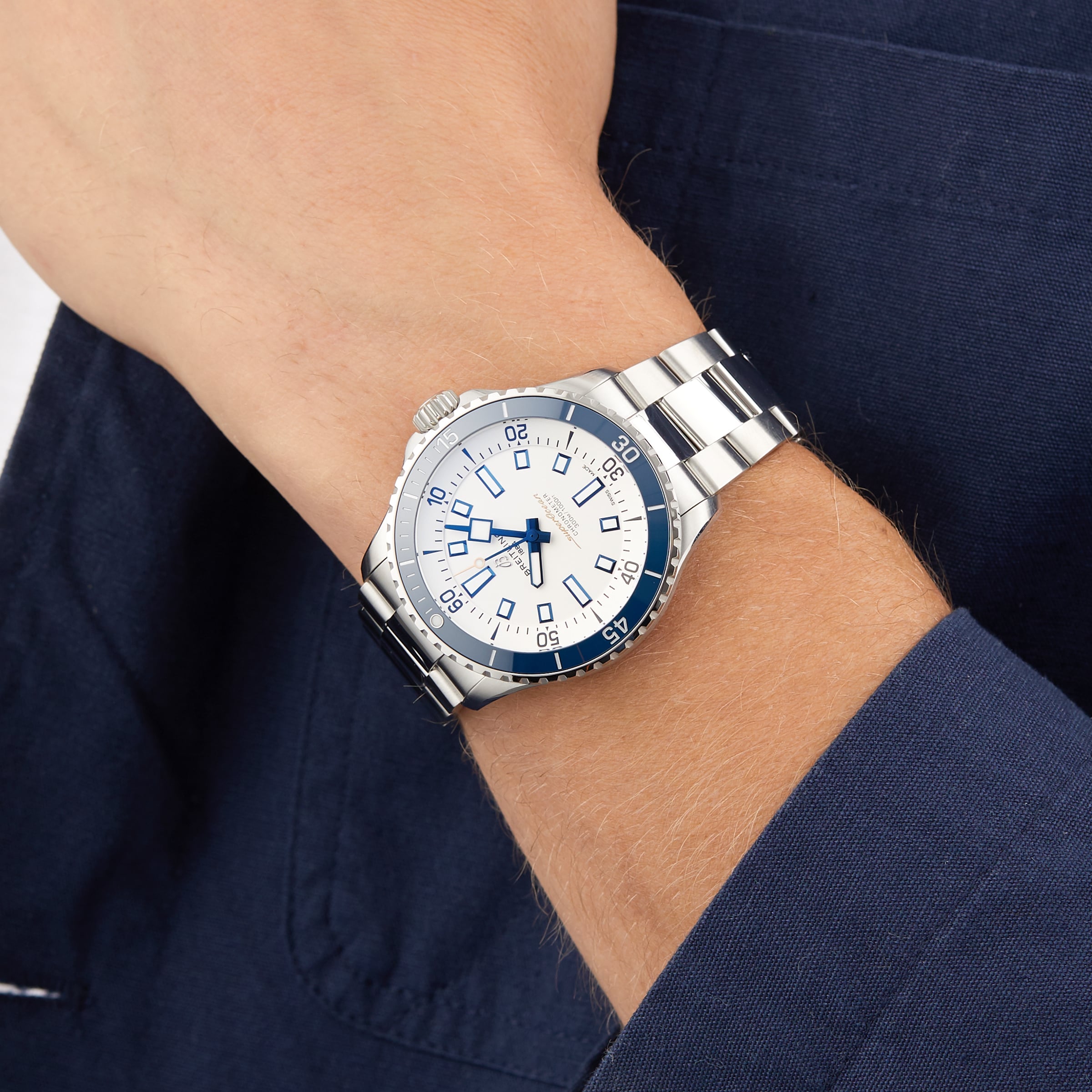 A person in a dark blue jacket wears the Breitling Superocean Automatic 42 dive watch with a white dial and blue markers.