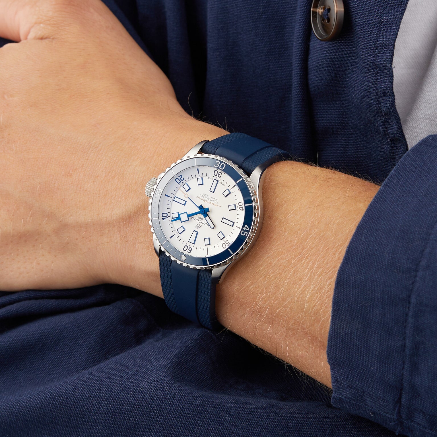 A person in a blue long-sleeve shirt wears the Breitling Superocean Automatic 42, featuring a blue and silver design, white dial, and blue strap.