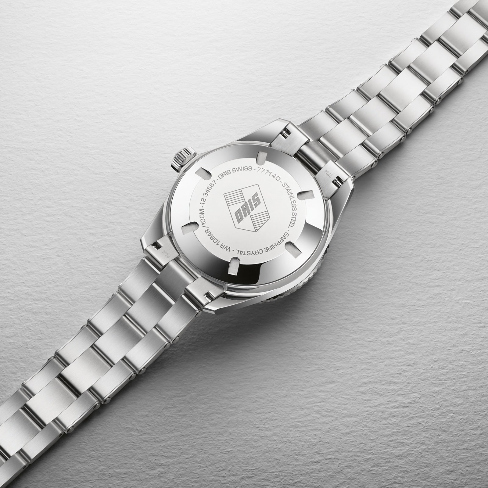 The Oris Divers Sixty-Five Cotton Candy, a silver metal wristwatch with an engraved Oris logo on the back case, rests on a textured surface.