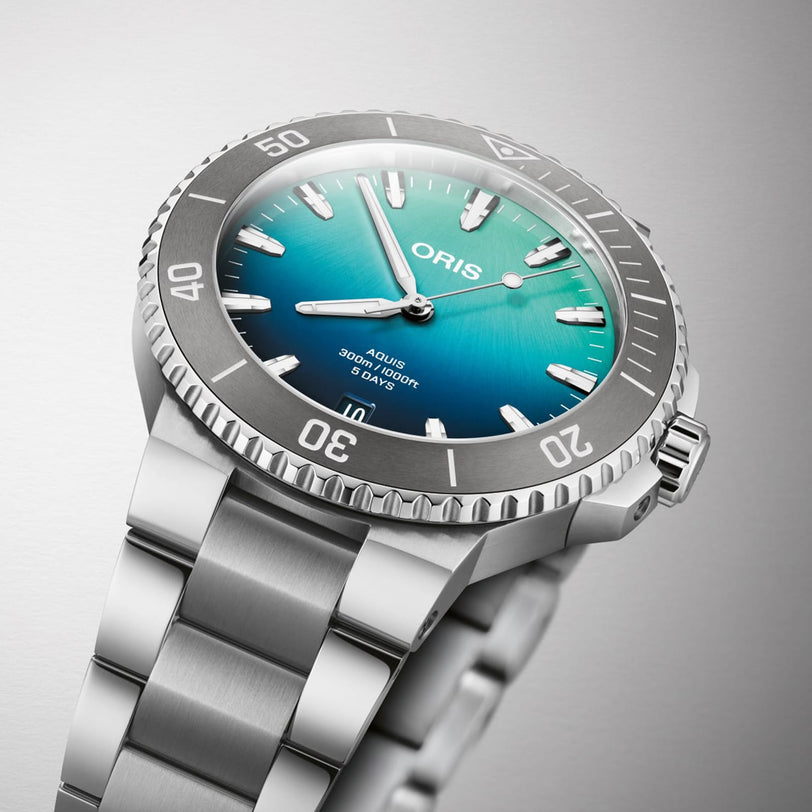 The Oris Great Barrier Reef Limited Edition IV is a stainless steel automatic watch featuring a blue gradient dial, silver hour markers, and a rotating bezel, showcased against a light grey background.