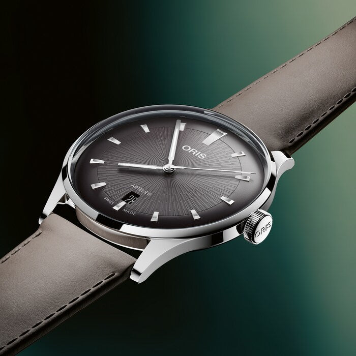 Stainless steel watch with black dial, silver hour markers, and gray leather strap against green background.