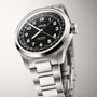 Silver stainless steel watch with black dial, Arabic numerals, date window, and matching bracelet band.
