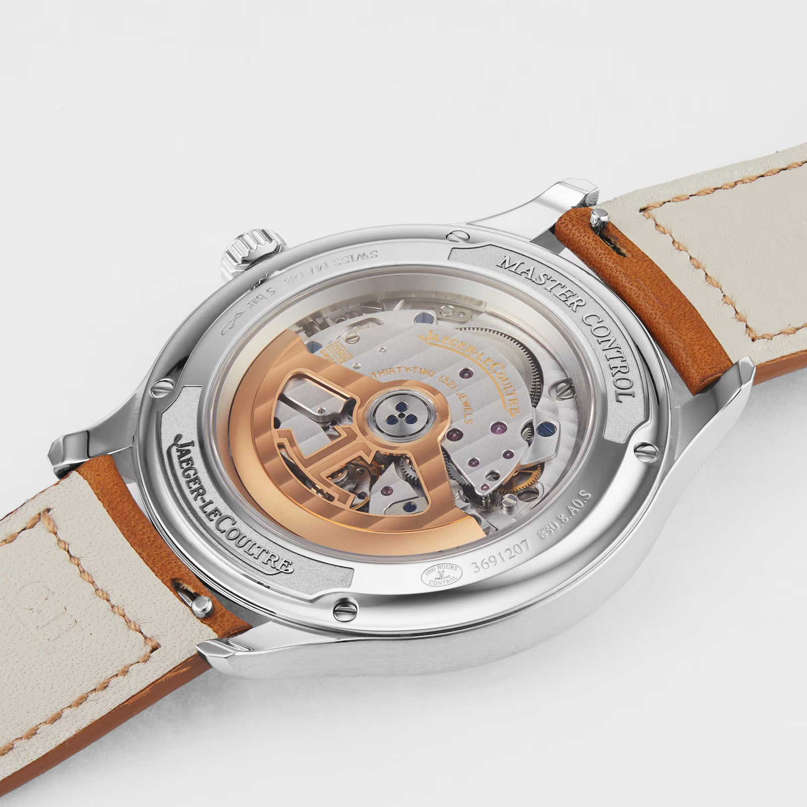 A close-up of the back of the Jaeger-LeCoultre Master Control Date watch reveals its intricate automatic movement through a transparent stainless steel case back, showcasing visible gears, a gold rotor, and a tan leather strap.
