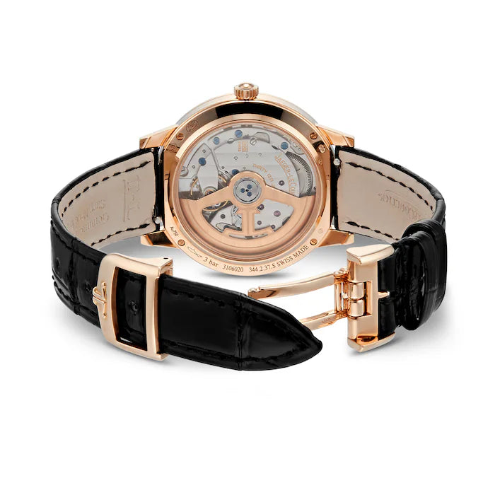 The Jaeger-LeCoultre Rendez-Vous Night & Day is a luxury women’s watch with a rose gold case, transparent case back revealing the movement, and a black leather strap with matching rose gold clasp.