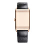 The Jaeger-LeCoultre Reverso Tribute Small Seconds is a rectangular gold Art Deco watch with a plain face, ridged frame, left-side crown, and a black textured leather strap.