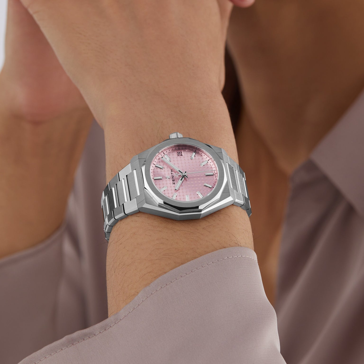 A person exudes urban sophistication, wearing Zenith’s Defy Skyline 36—a silver wristwatch marked by the iconic four-pointed star on its pink face—complemented by a light mauve long-sleeved shirt.