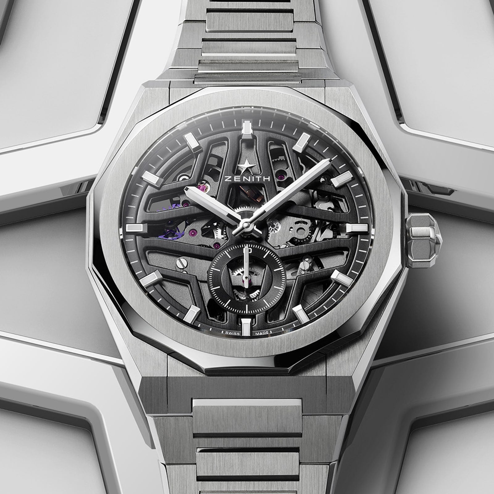 A Zenith Defy Skyline Skeleton watch with a stainless steel bracelet and skeleton dial, showcasing the El Primero 3620 movement, is placed on a geometric metallic surface.