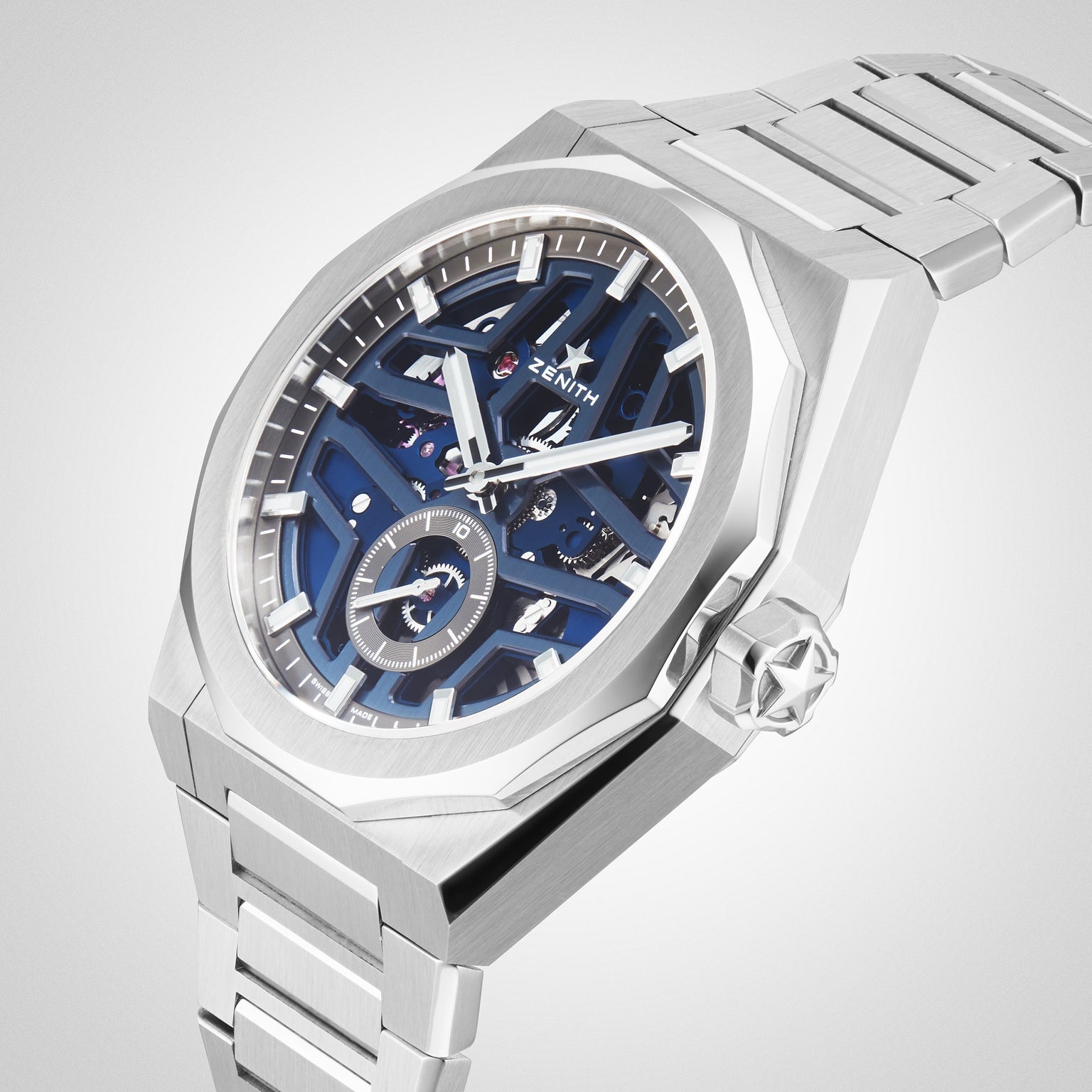 The Zenith Defy Skyline Skeleton wristwatch, featuring a blue skeleton dial with exposed gears and a stainless steel bracelet, embodies urban sophistication against a light backdrop.