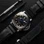 A close-up of the Panerai Submersible es men’s dive watch with a titanium case, black dial with blue accents, date display, and rubber strap, surrounded by branded watch tools on a dark surface.