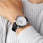 Wearing a light gray ribbed sweater, a person showcases the Panerai Luminor Chrono with a white dial, black leather strap, multiple subdials, and visible power reserve indicator on their left wrist.