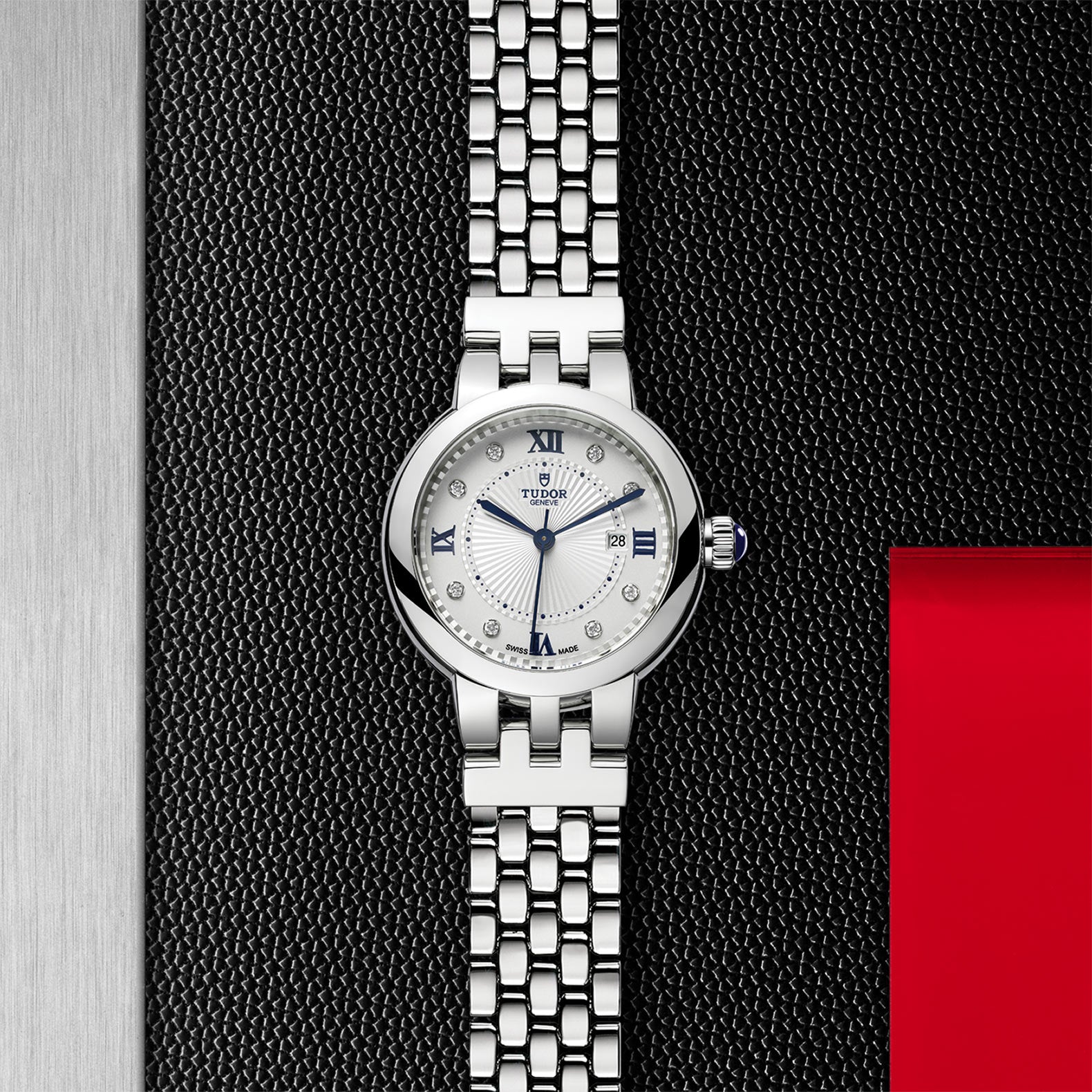 A TUDOR Clair de Rose silver wristwatch with a white face and diamond hour markers, shown on a textured black background.