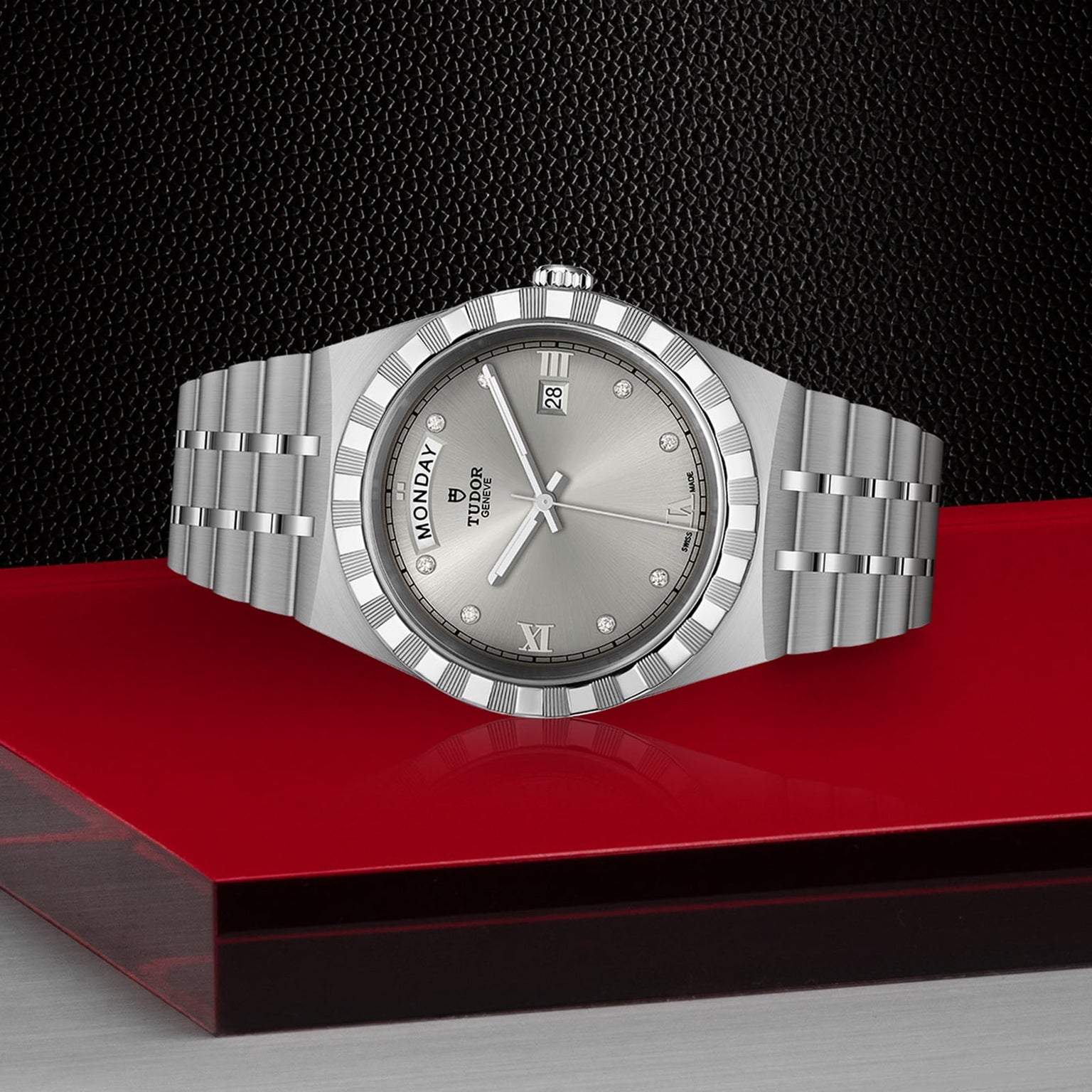 A silver TUDOR Royal wristwatch featuring diamond hour markers, day-date display, and integrated bracelet rests on a red and black texture—embodying the automatic sport-chic style of the Royal by TUDOR.