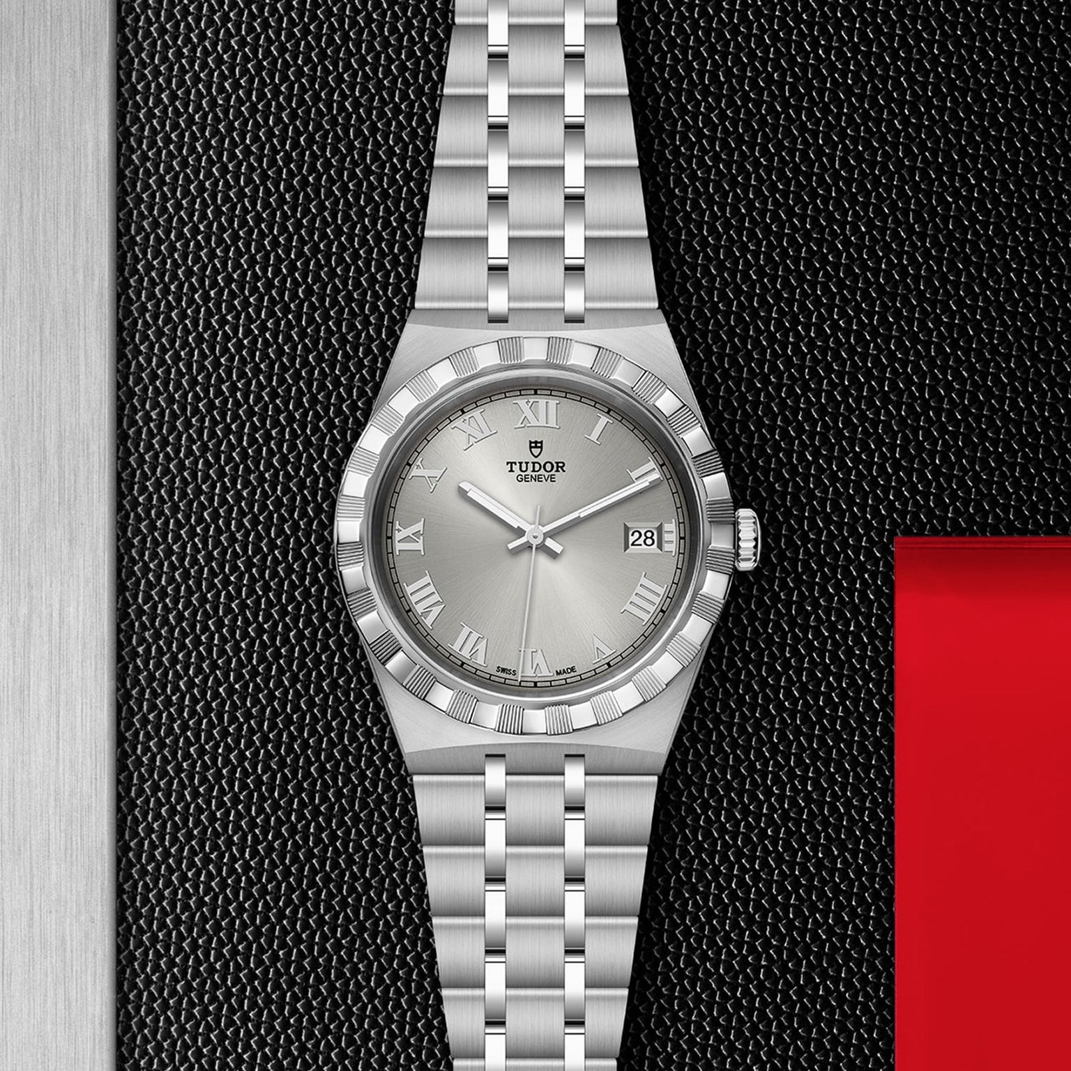 A TUDOR Royal wristwatch with a stainless steel and gold band, Roman numerals, and date window is displayed on a textured black surface.