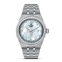 The TUDOR Royal is a silver wristwatch with a stainless steel band, diamond-set bezel, mother-of-pearl dial, Roman numerals, and a date window at 3 o’clock.