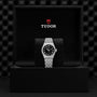 A TUDOR Royal wristwatch, featuring a black dial with Roman numerals, is presented on a cushion inside a black TUDOR box, highlighting the sport-chic elegance of this automatic stainless steel and gold timepiece.