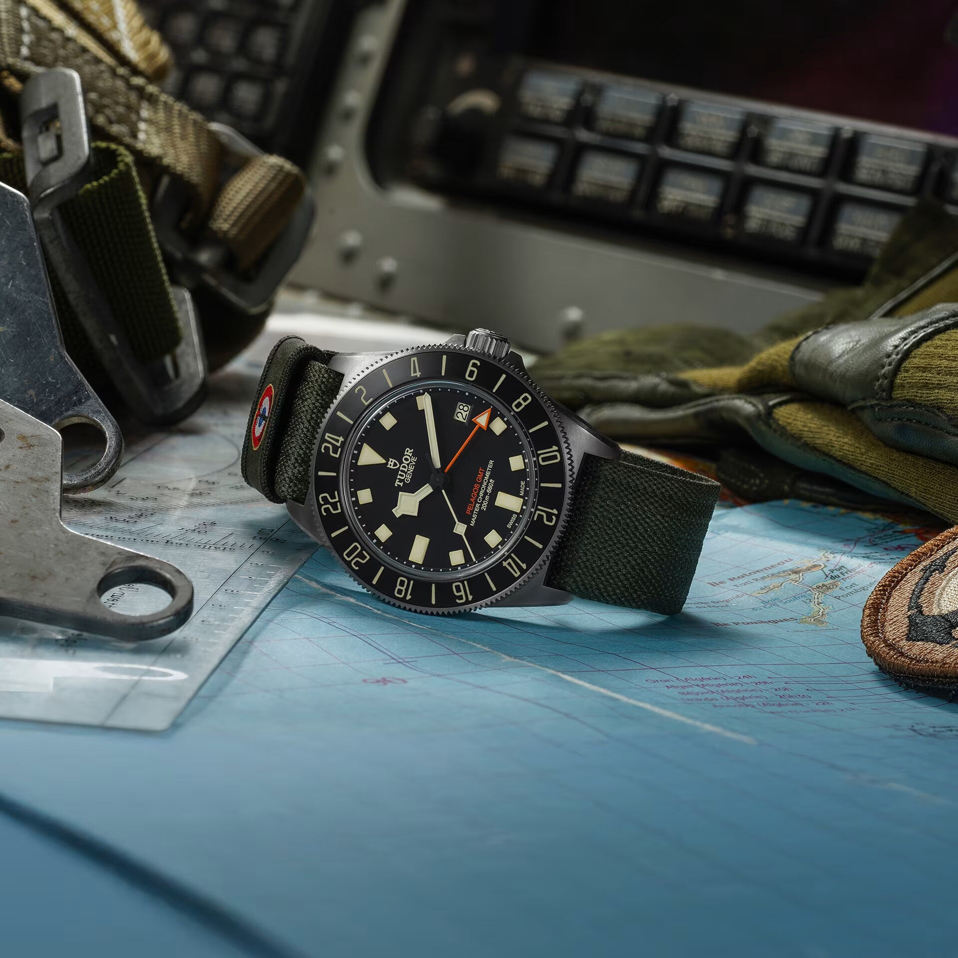 The TUDOR Pelagos FXD GMT, featuring a green strap, is displayed on a map surrounded by flight gear and cockpit controls.