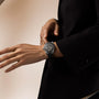 Black watch with dark dial and bezel worn on wrist over black sleeve.