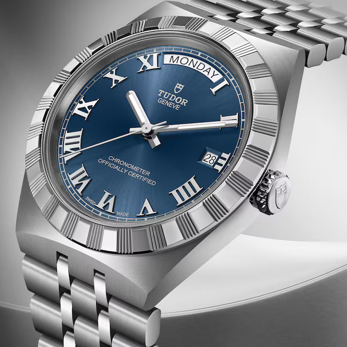 Tudor Royal stainless steel watch with blue dial, Roman numerals, day-date window, and matching metal bracelet.