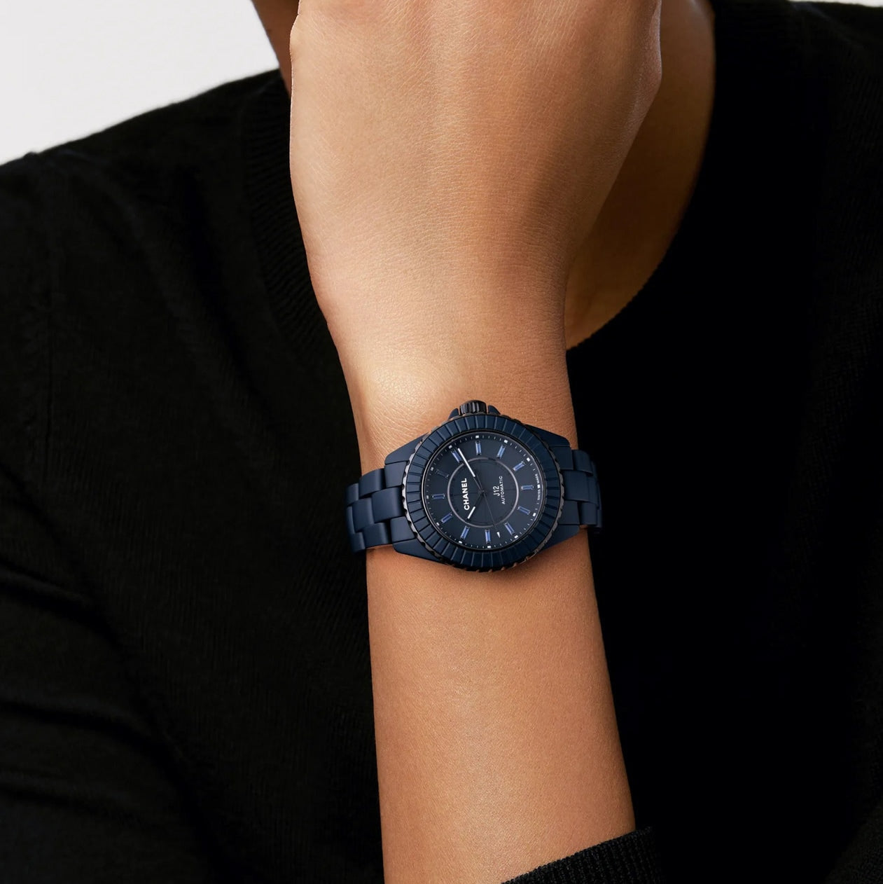 A person wearing a Chanel J12 Bleu Watch Caliber 12.1, 38 mm on their left wrist, dressed in a black top.