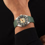 A person wears a DOXA Army Bronze by DOXA with a green strap, beige and black dial, orange accents, and a stainless steel uni-directional rotating bezel, paired with a black long-sleeve shirt.