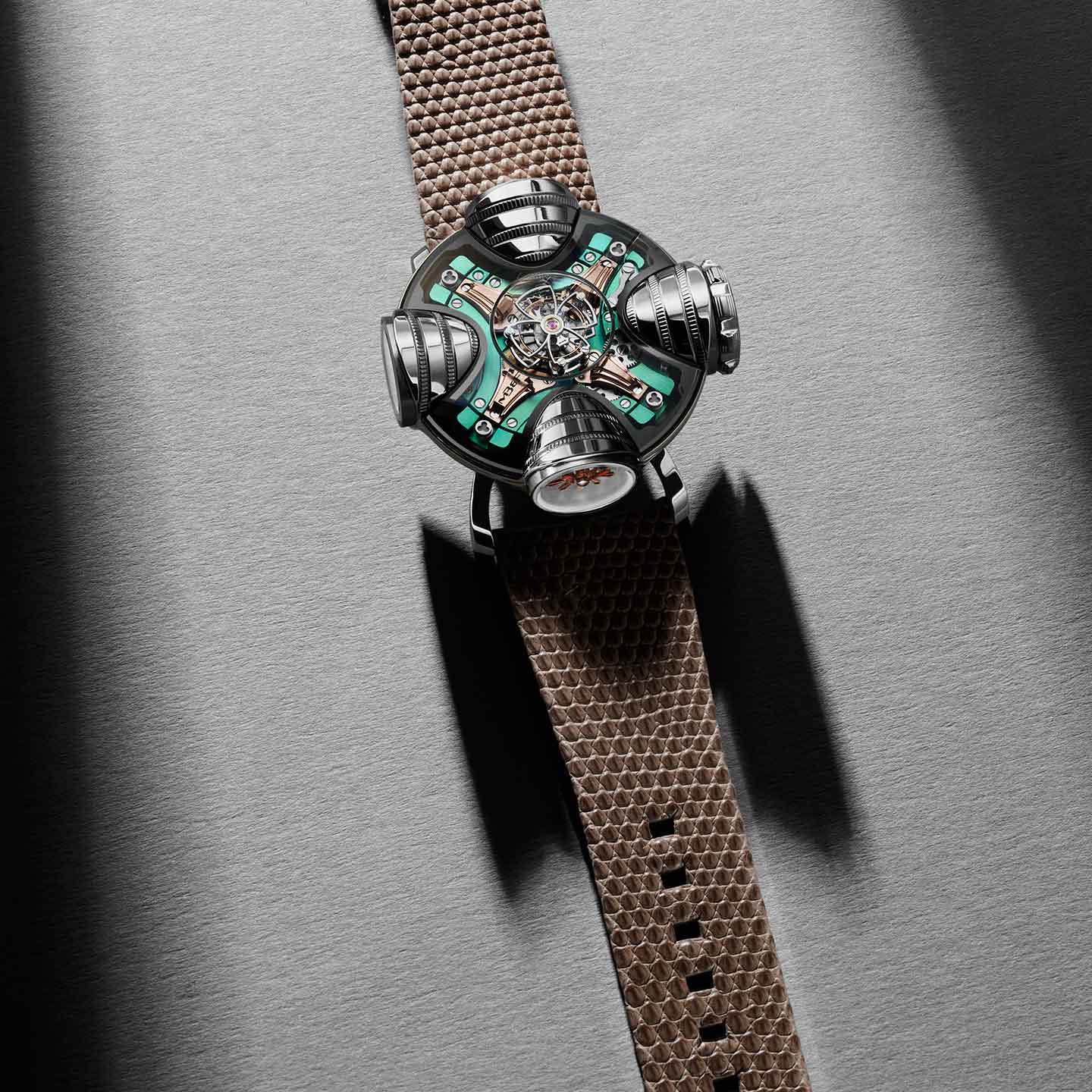The MB&F HM11 Art Deco is a futuristic watch with a metallic, skeletonized multi-dial face showcasing exposed gears and green circuit-like details, paired with a brown textured strap, set against a gray surface with dramatic shadows.