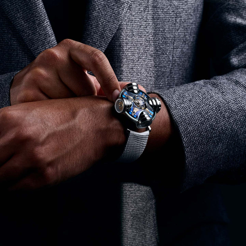A person in a gray suit adjusts the MB&F HM11 Art Deco wristwatch, featuring a metallic band and skeletonised dial, highlighting its unique mechanical design on their left wrist.