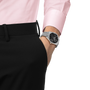 Silver-tone watch with black dial and metal bracelet worn on wrist with pink shirt and black pants.