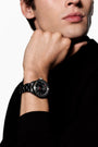 Black ceramic sports watch with dark dial worn on man's wrist against black sleeve.