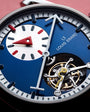 Blue watch dial with white and red hands, white subdial with red hand, Louis Erard text, and exposed tourbillon mechanism.
